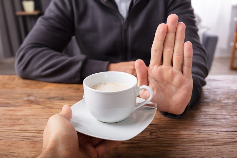 person holding their hand up to refuse a cup of coffee
